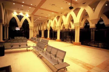 Large airport waiting hall with rows of metal seats, pointed arches and glazed service areas.